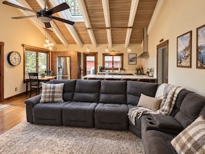 Ein modernes Wohnzimmer mit einem Ecksofa, einem Essbereich mit Tisch und Stühlen, einer Küche mit einer großen Kochinsel und einem Deckenventilator.
