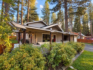 Ein eingeschossiges Haus mit Veranda, umgeben von einem Holzzaun und üppiger Bepflanzung.