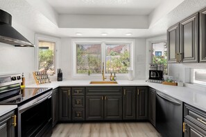 A modern kitchen with dark cabinetry, a stainless steel range hood, and a double sink. - Luxury Red Rock Retreat:  3 Bed/ 2 Bath With Heated Pool & Spa, Game Room (Sedona)