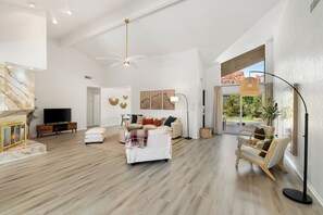 A spacious living room with a fireplace, a sofa set, a television, and a large window offering a view of the outdoors. - Luxury Red Rock Retreat:  3 Bed/ 2 Bath With Heated Pool & Spa, Game Room (Sedona)