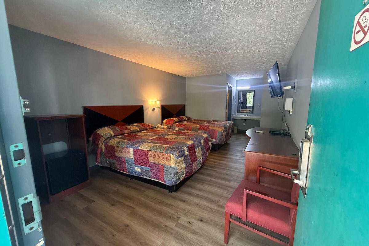 Habitación de hotel con dos camas, un escritorio, un espejo y un televisor.