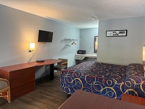 Habitación de hotel con cama, escritorio, silla, televisión y una pequeña kitchenette.
