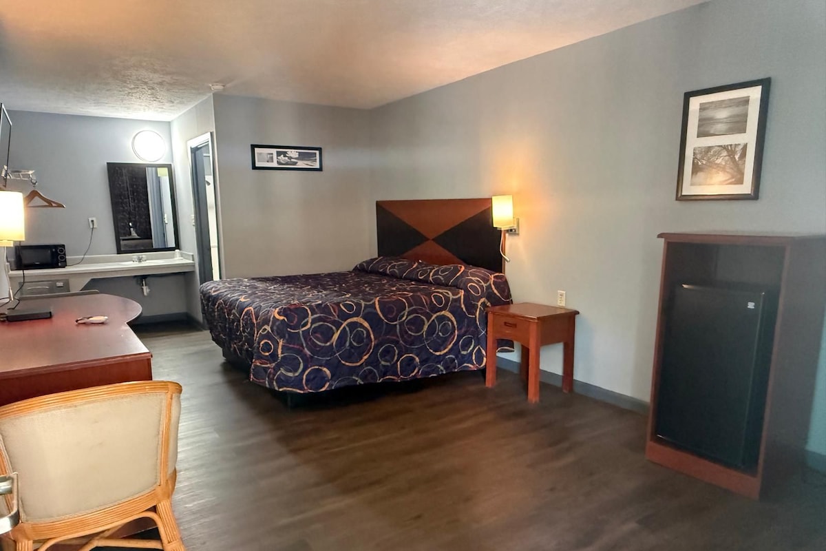 Habitación de hotel con cama, mesita de noche, lámpara, escritorio, silla y armario.