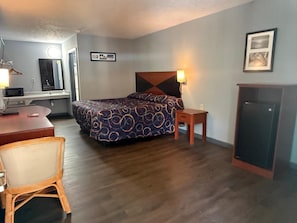 Habitación de hotel con cama, mesita de noche, lámpara, escritorio, silla y armario.