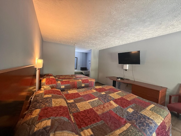 Habitación de hotel con dos camas, un escritorio, un televisor y una lámpara.