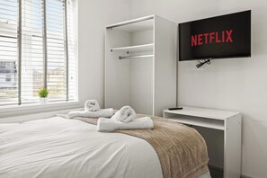 Une chambre d’hôtel avec un lit, un téléviseur fixé au mur et une fenêtre avec des stores.