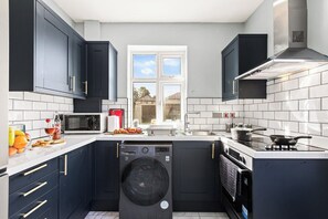 A modern kitchen with dark cabinets, a built-in washing machine, a microwave, and a stove. - 4 Doubles, 4 En-Suites & a Big Garden – Sleeps 8 (Ashton-on-Ribble)