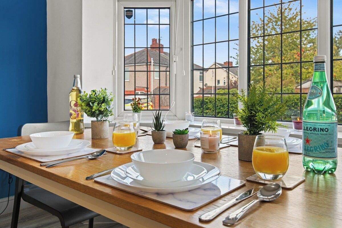 A breakfast table set with white dishes, glasses, and a bottle of mineral water.