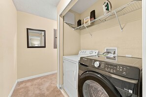 A laundry room with a front-loading washer and dryer, a mirror, and a shelf with laundry supplies. - Family 4br, Private Pool, Resort Amenities (Kissimmee)