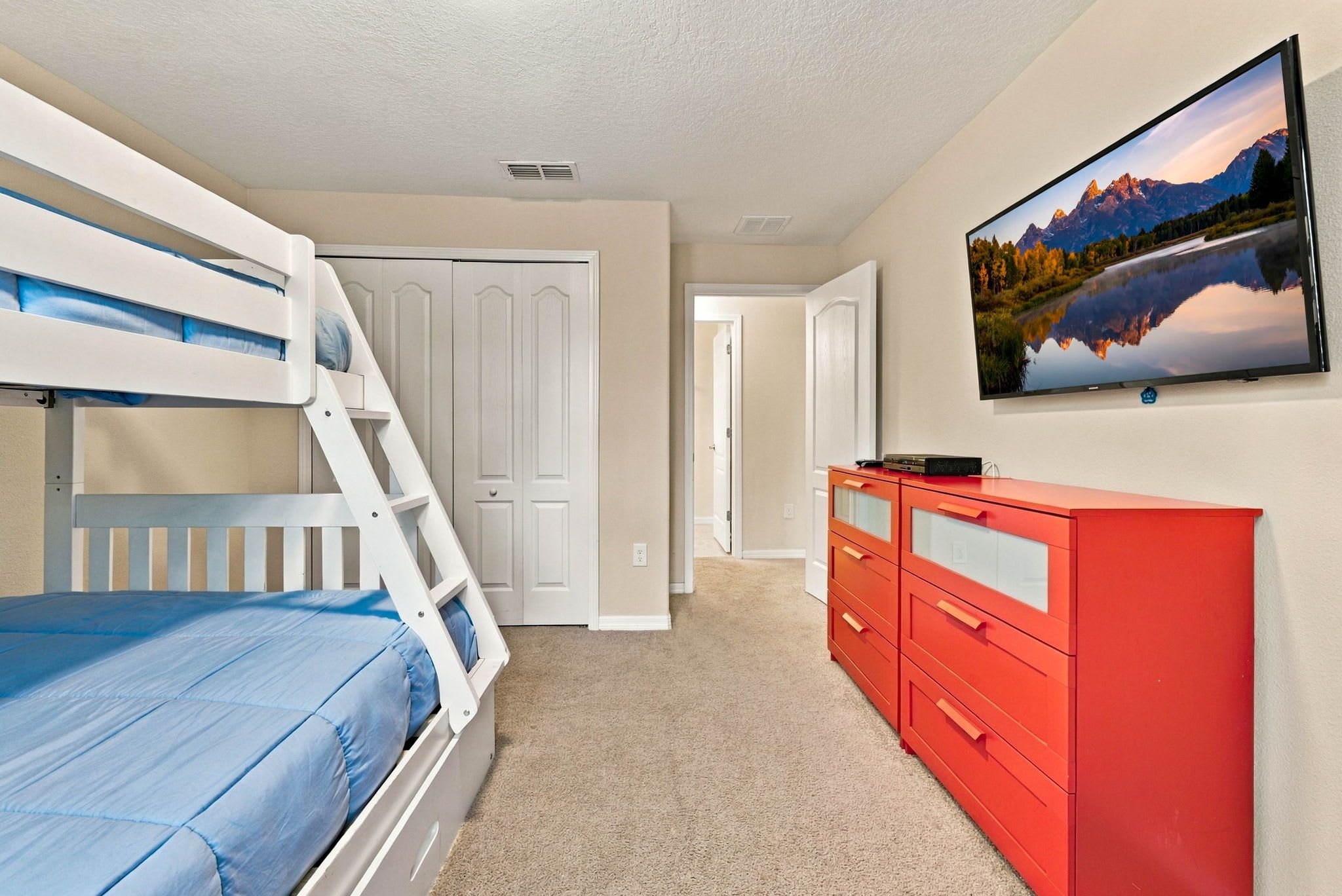 A bedroom with bunk beds, a red dresser, and a wall-mounted TV.