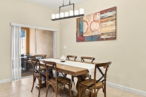 A dining area with a wooden table and chairs, a chandelier, and a large abstract painting on the wall. - Family 4br, Private Pool, Resort Amenities (Kissimmee)