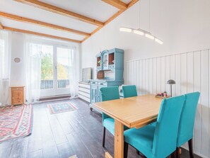 Ein Essbereich mit einem Holztisch, smaragdgrünen Stühlen, einem blauen Schrank und Blick durch eine Glastür.