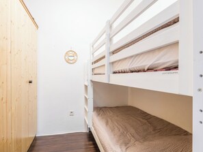 Ein kleiner, kompakter Raum mit zwei Etagenbetten, einem Holzschrank und einer Wandleuchte.
