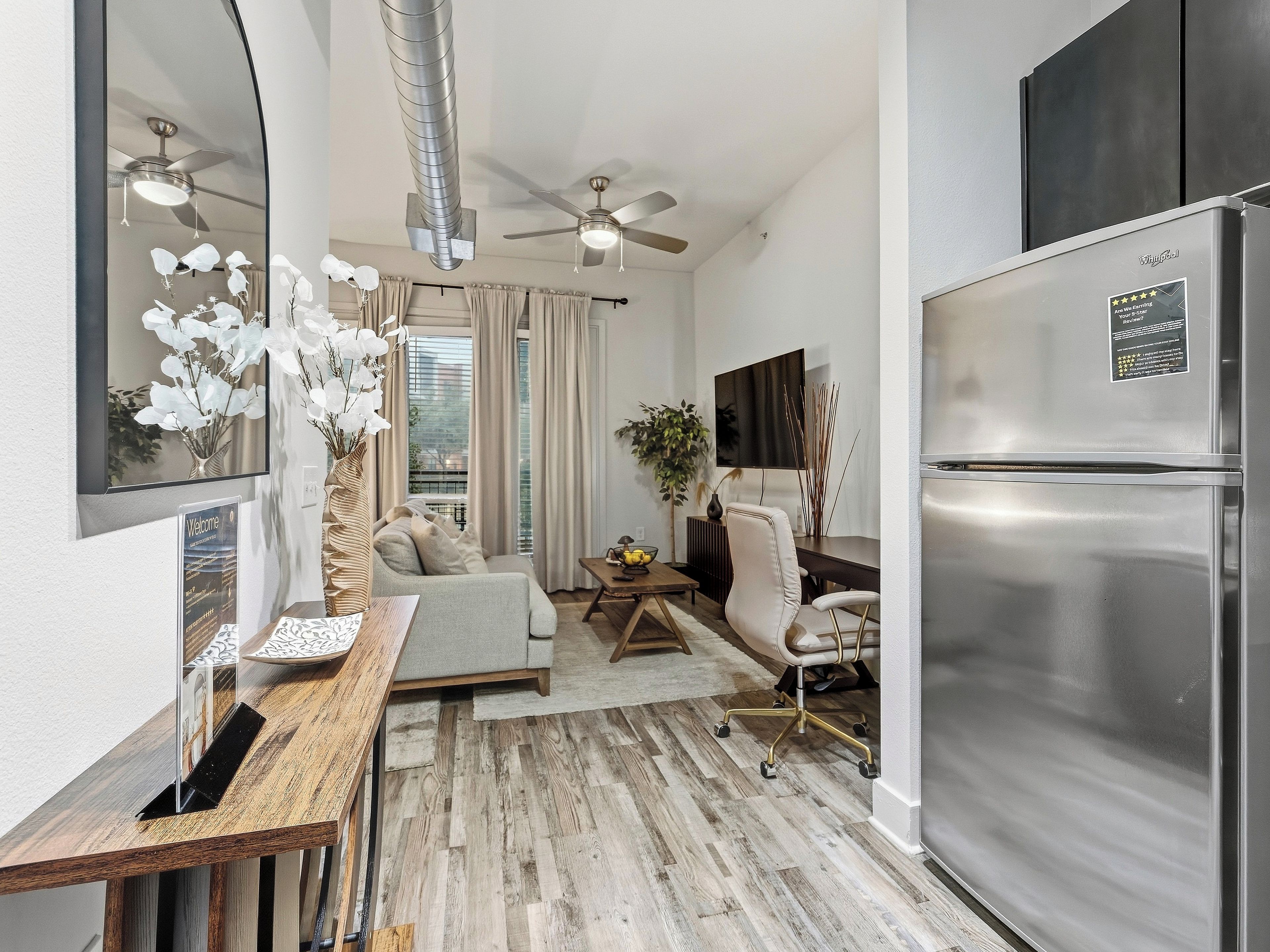 Una cocina moderna con un refrigerador de acero inoxidable, un comedor con mesa y sillas de madera, y una sala de estar con sofá y ventilador de techo.