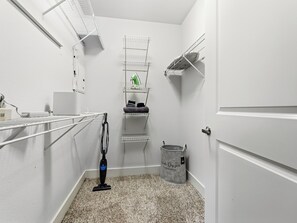 A laundry room with a vacuum cleaner, shelves with towels, and a trash can. - 1BR,FREE Parking.Near AAC, 182 (Dallas)