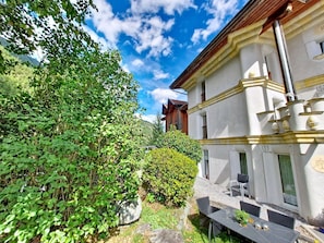 Ein Gebäude mit Balkon, einem Tisch mit Stühlen und einem Garten mit Grünflächen.