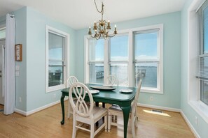 Uma sala de jantar com uma mesa verde, cadeiras brancas e um candelabro.