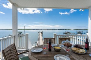 Eine Holzterrasse mit gedecktem Tisch, mit Blick auf ruhiges Wasser, Stege und Boote.
