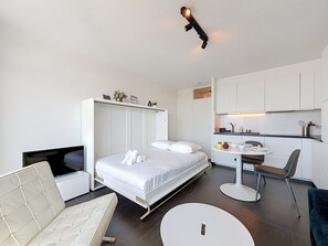 A modern hotel room with a bed, a sofa, a small round table, a chair, and a kitchenette. - Astrid with parking and seaview by Interhome (Bredene)