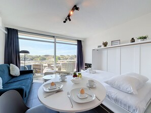 A hotel room with a bed, a sofa, a dining table with breakfast set, and a large window with a view of the city. - Astrid with parking and seaview by Interhome (Bredene)
