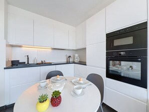 A modern kitchen with white cabinetry, a dining table set with plates, cups, and a pineapple centerpiece. - Astrid with parking and seaview by Interhome (Bredene)