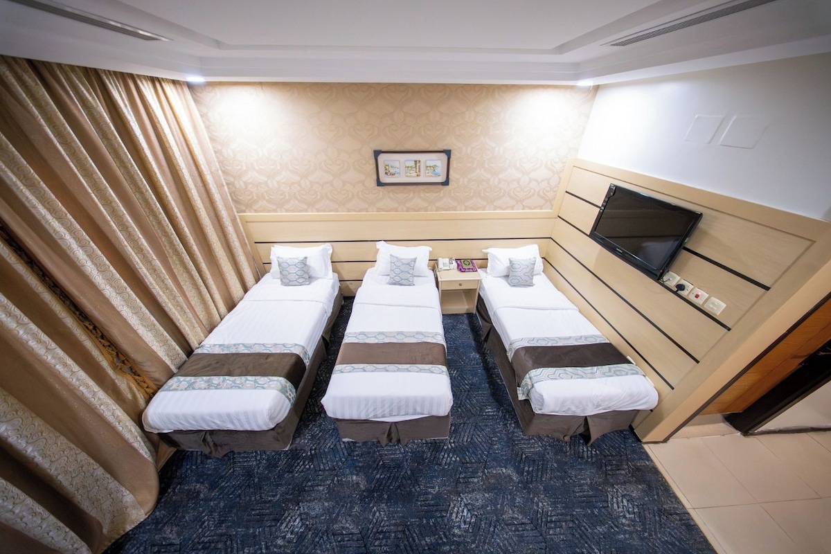 A hotel room with four single beds, a television, a small desk, and a patterned carpet.