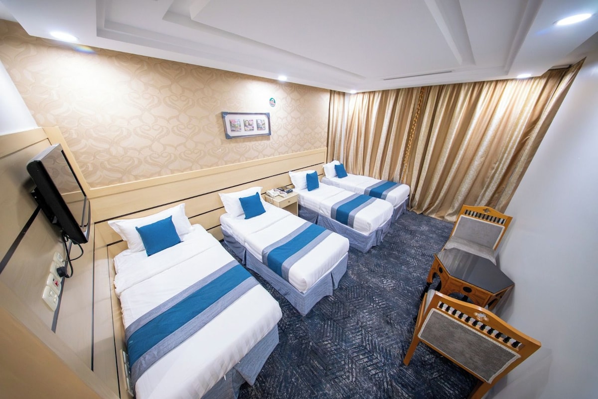 A hotel room with three single beds, a desk, a chair, and a television.