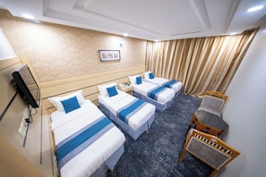 A hotel room with three single beds, a desk, a chair, and a television. - multazam Hotel (Makkah)