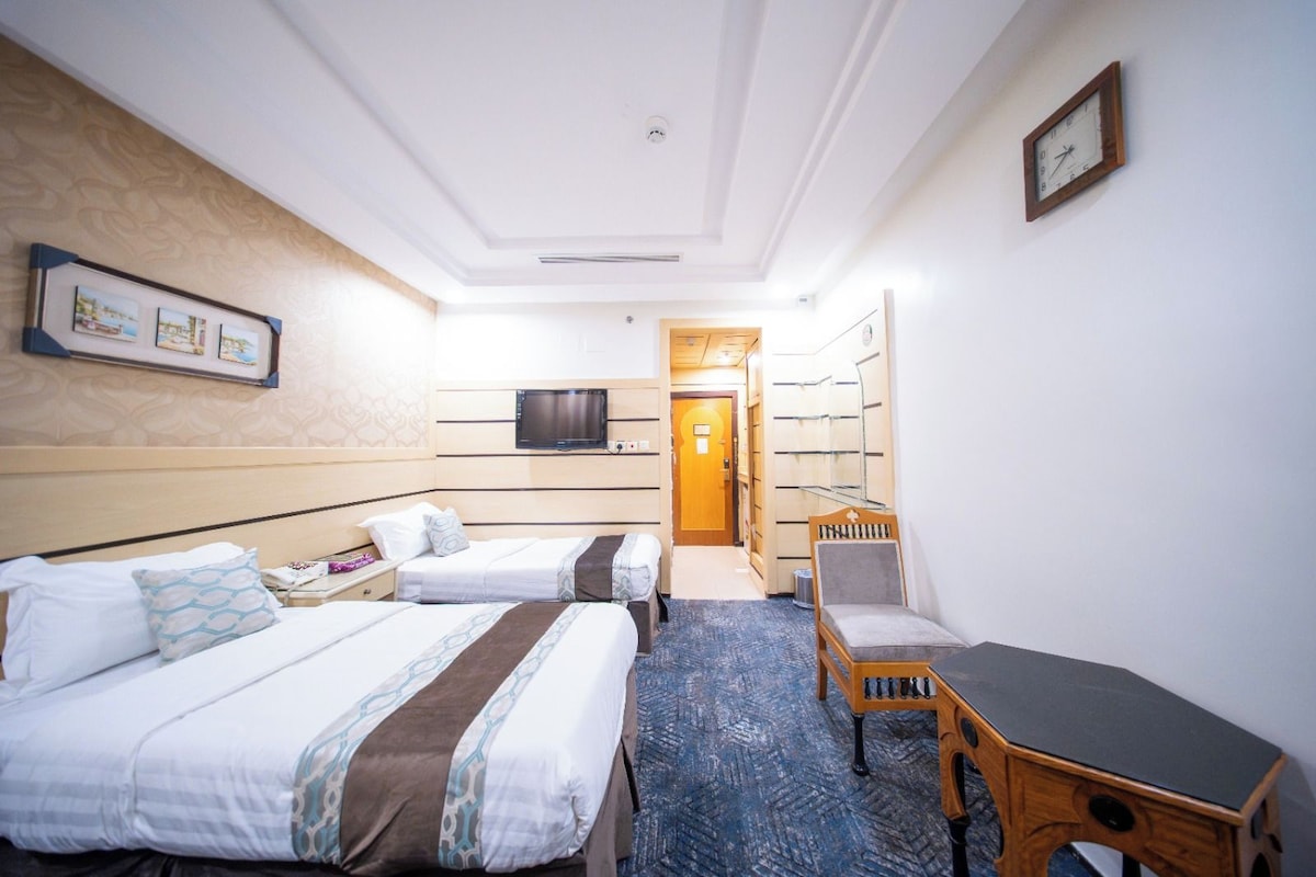 A hotel room with two beds, a desk, a chair, a television, and a door leading to a hallway.