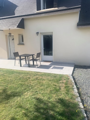 Eine Terrasse mit Tisch, Stühlen, einer Tür und einem kleinen Fenster.