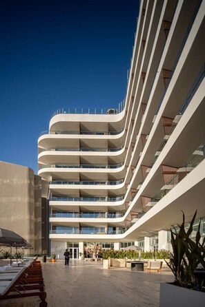 Hotel moderno de vários andares com fachada curva, área de estar ao ar livre e um pátio central.