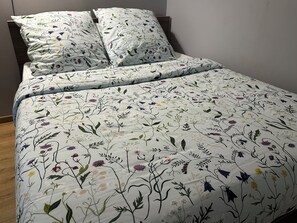 A bed with a floral-patterned bedspread and two pillows. - Elegant house with a garden, terraces, and parking on the outskirts of Fontainebleau (Saint-Pierre-lès-Nemours)