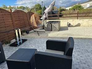 Une terrasse extérieure avec un espace salon, un fauteuil suspendu et une table.
