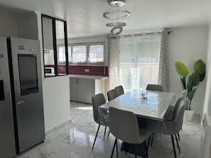 A modern kitchen with a refrigerator, cabinets, and a dining table with chairs. - Elegant house with a garden, terraces, and parking on the outskirts of Fontainebleau (Saint-Pierre-lès-Nemours)