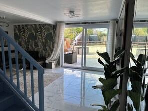 Un vaste espace de vie comprenant un escalier, une grande porte-fenêtre coulissante donnant sur une terrasse extérieure et un plafond agrémenté d’un luminaire décoratif.