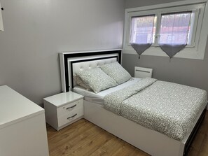 Une chambre à coucher avec un lit, des tables de chevet, une commode et une fenêtre avec des stores.