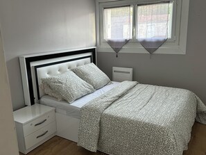 Ein Schlafzimmer mit einem Bett, einem Nachttisch, einer Kommode und einem Fenster mit Vorhängen.