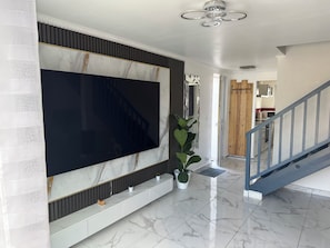 A modern interior with a large flat-screen TV mounted on a wall, a staircase with a metal railing, and a potted plant. - Elegant house with a garden, terraces, and parking on the outskirts of Fontainebleau (Saint-Pierre-lès-Nemours)