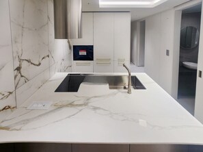 Eine moderne Küche mit weißer Marmorarbeitsplatte, Edelstahlspüle und eingebautem Backofen.