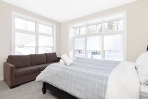A bedroom with a bed, a brown sofa, and large windows. - 20 Mins to Arrowhead Family Friendly Getaway (Huntsville)