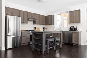 A modern kitchen with dark wood cabinets, a stainless steel refrigerator, and a bar area with stools. - 20 Mins to Arrowhead Family Friendly Getaway (Huntsville)