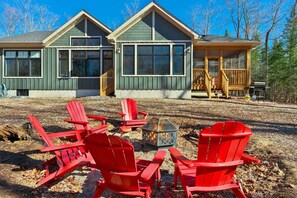 Une cabane dotée d’une terrasse, de grandes fenêtres et de chaises Adirondack rouges devant l’entrée.