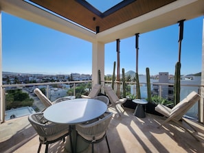 A balcony with a table and chairs, overlooking a cityscape with buildings and a mountain. - Ameth- Apartments w/ Rooftop Pool & Gym (Cabo San Lucas)