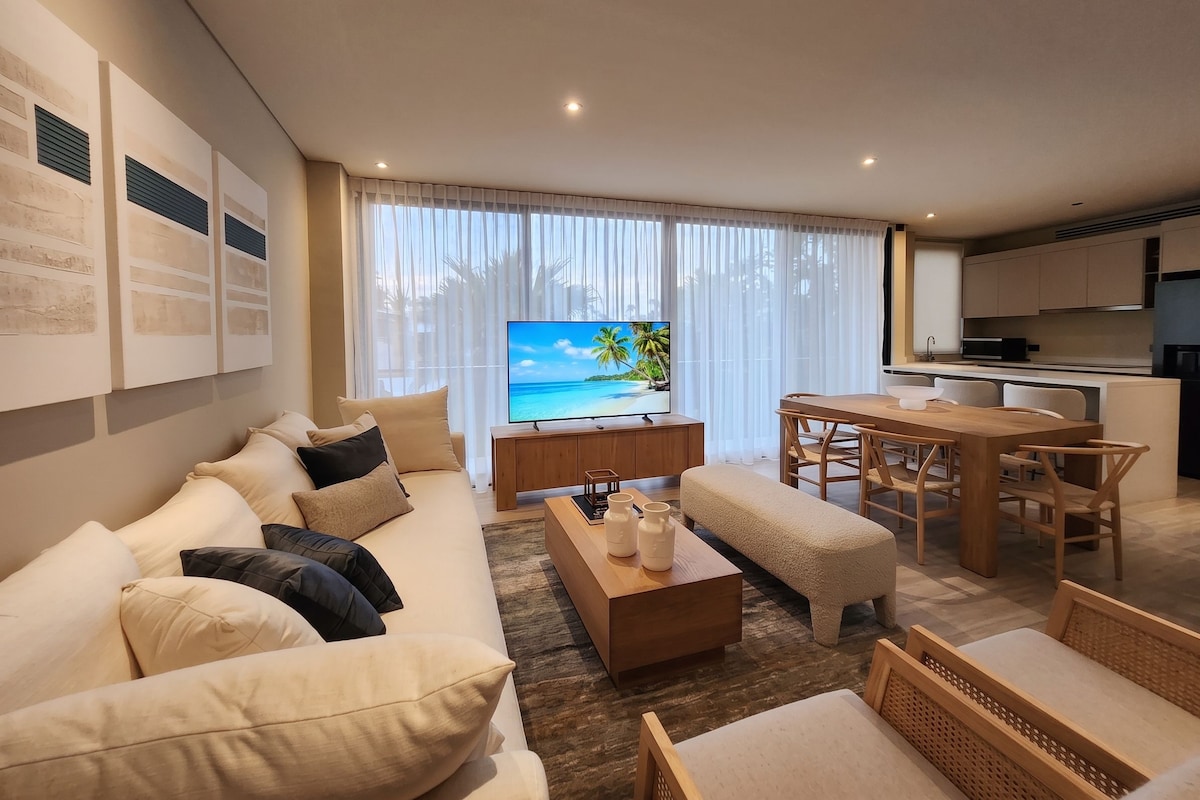 Ein modernes Wohnzimmer mit einer Couch, einem Couchtisch und einem Fernseher, der eine tropische Strandlandschaft zeigt.