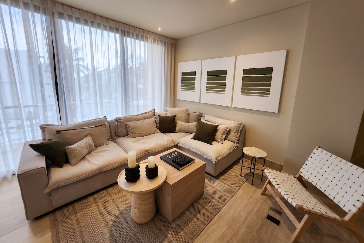 Ein modernes Wohnzimmer mit einer Eckcouch, einem Couchtisch und einem kleinen Beistelltisch. Oberhalb der Couch befinden sich abstrakte Wandbilder.