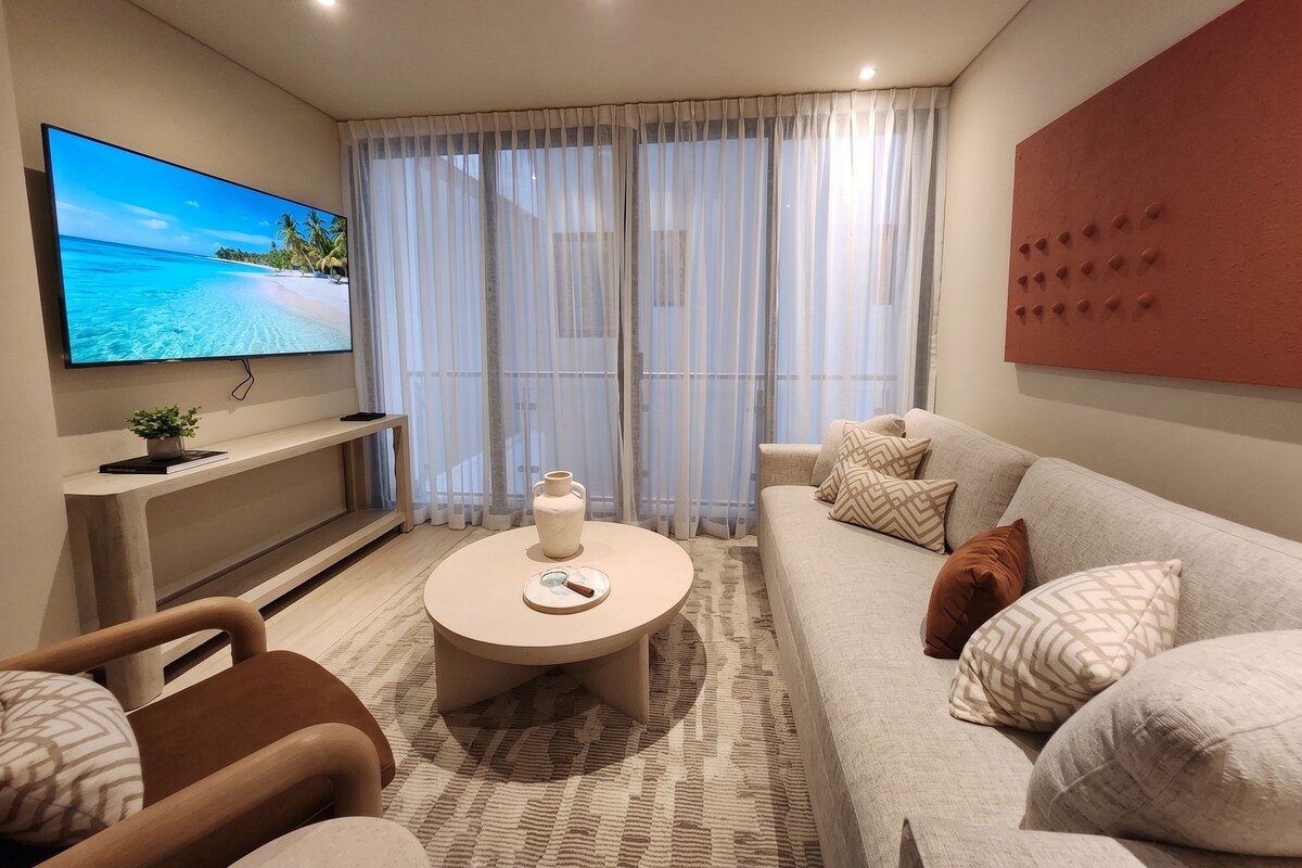 Ein modernes Wohnzimmer mit einem Flachbildfernseher, einem runden Couchtisch, einer Couch und einem gemusterten Teppich.