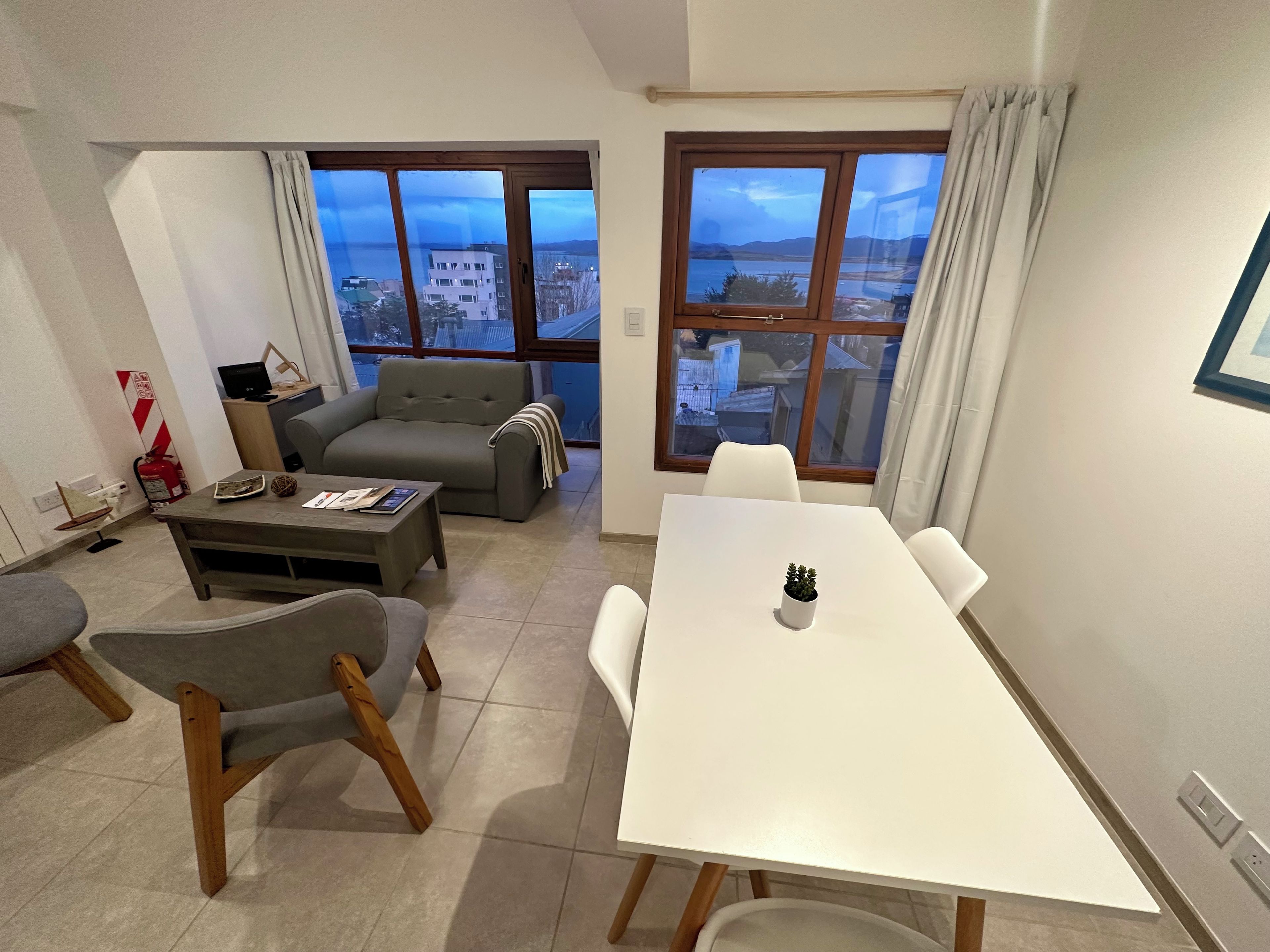 Una sala de estar moderna con sofá, una mesa de comedor y vistas de la ciudad a través de grandes ventanales.