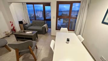 Una sala de estar moderna con sofá, una mesa de comedor y vistas de la ciudad a través de grandes ventanales.