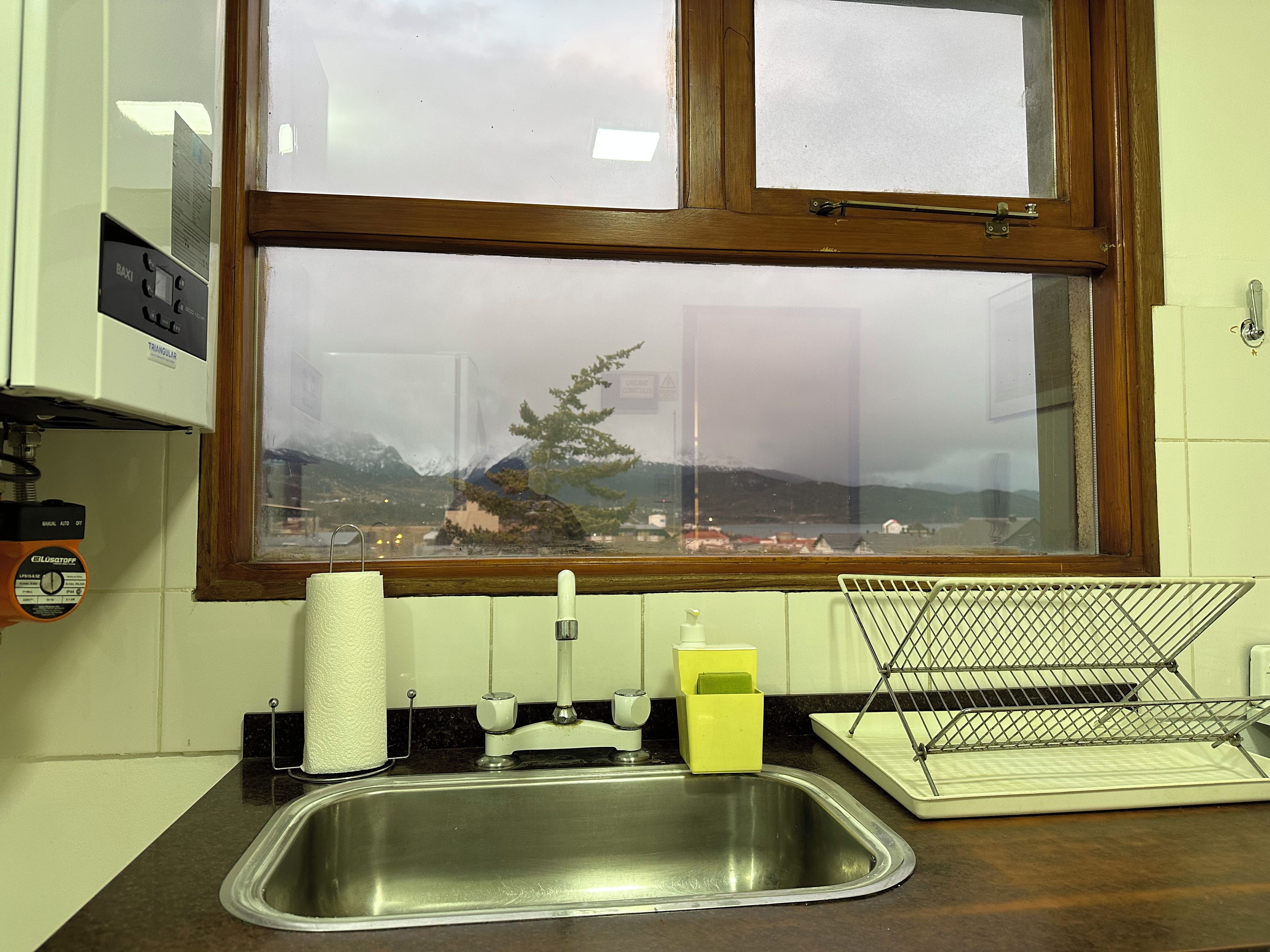 A kitchen with a stainless steel sink, a window with a view of a mountain, and a paper towel dispenser.