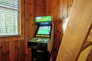 A video game machine in a room with wooden walls and a window. - Classic! Away From It All! Hot Tub-Firepit-Arcade! (Broken Bow)